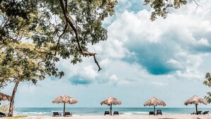 Una spiaggia con ombrelloni di paglia e lettini, cielo sereno e mare calmo.