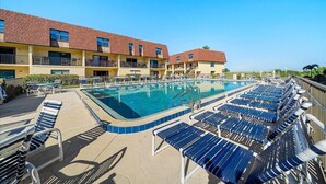 Un espace piscine avec des chaises longues bleues et un bâtiment aux murs jaunes et aux toits rouges.