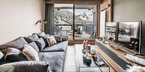 A modern living room with a grey sofa, a coffee table with drinks and snacks, a TV, and a view of mountains through large windows. - 200m from ski slopes, 1st floor, ski locker, 50m², Tignes (Tignes)