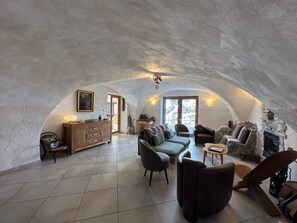 Een gezellige, gewelfde woonkamer met een open haard, comfortabele zithoek en een houten kast.
