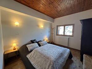 Een slaapkamer met een groot bed, twee bedlampen, een raam met uitzicht en een houten plafond.