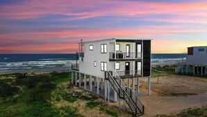 Una casa moderna frente al mar, de dos pisos, con una escalera que lleva a la parte superior y vistas al océano.