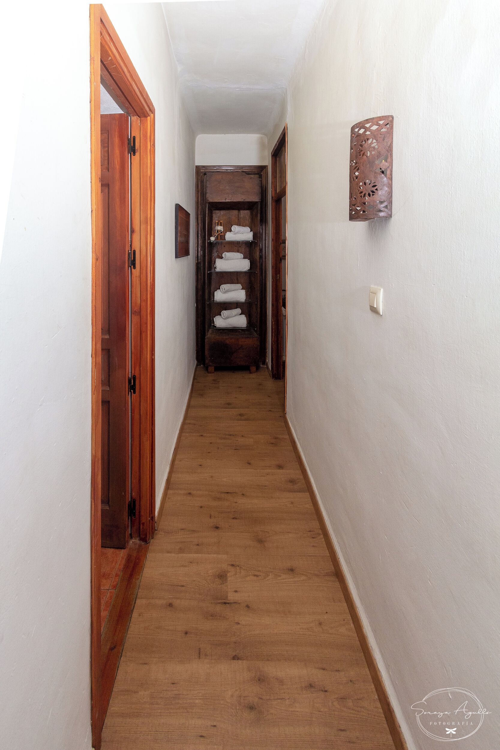 Un couloir étroit avec un plancher en bois, des murs blancs et une porte en bois sur le côté gauche.