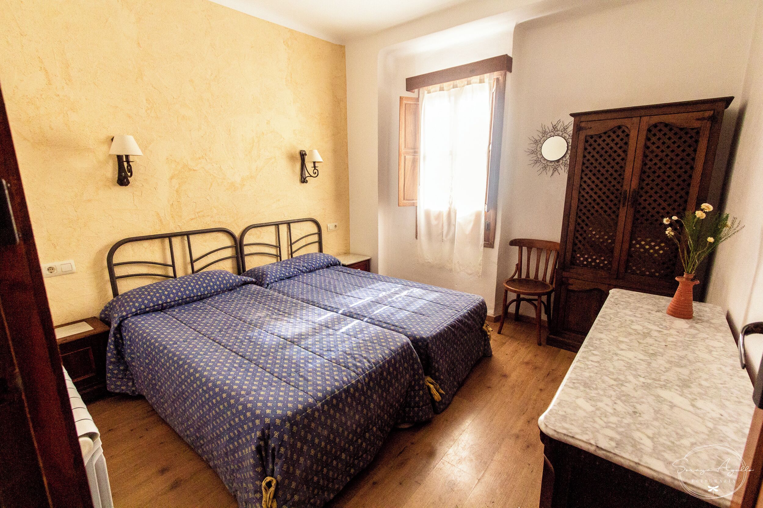Un dormitorio con dos camas, un armario de madera, una mesita y una silla.