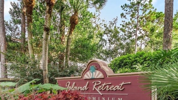 Un letrero que dice 'Island Retreat' con un logo de palmera, rodeado de exuberante follaje y árboles.