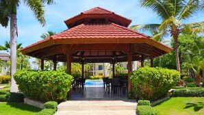A covered pavilion with a tiled roof, surrounded by well-maintained greenery and a pool area. - Punta Cana - Apartment - Sleeps 4 - Pool - Hot Tub (Punta Cana)
