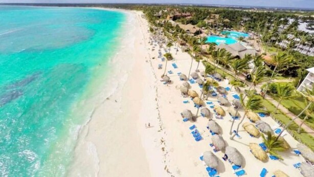 A beach resort with a clear turquoise sea, white sand, and a pool area with umbrellas and lounge chairs. - Punta Cana - Apartment - Sleeps 4 - Pool - Hot Tub (Punta Cana)
