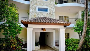 A covered entrance with a stone wall, white columns, and a tiled roof. - Punta Cana - Apartment - Sleeps 4 - Pool - Hot Tub (Punta Cana)
