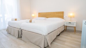 Un lit double avec une tête de lit en bois, deux tables de chevet avec des lampes et une fenêtre avec des rideaux légers.