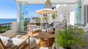 Un balcón moderno con vista al mar, amueblado con un sofá, sillas y una mesa.