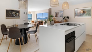 Una cocina moderna con una isla central, comedor con sillas, luces colgantes y obras de arte en las paredes.