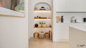 Una cocina moderna con armarios blancos, una estantería empotrada con objetos decorativos y una isla central con un lavamanos y utensilios.