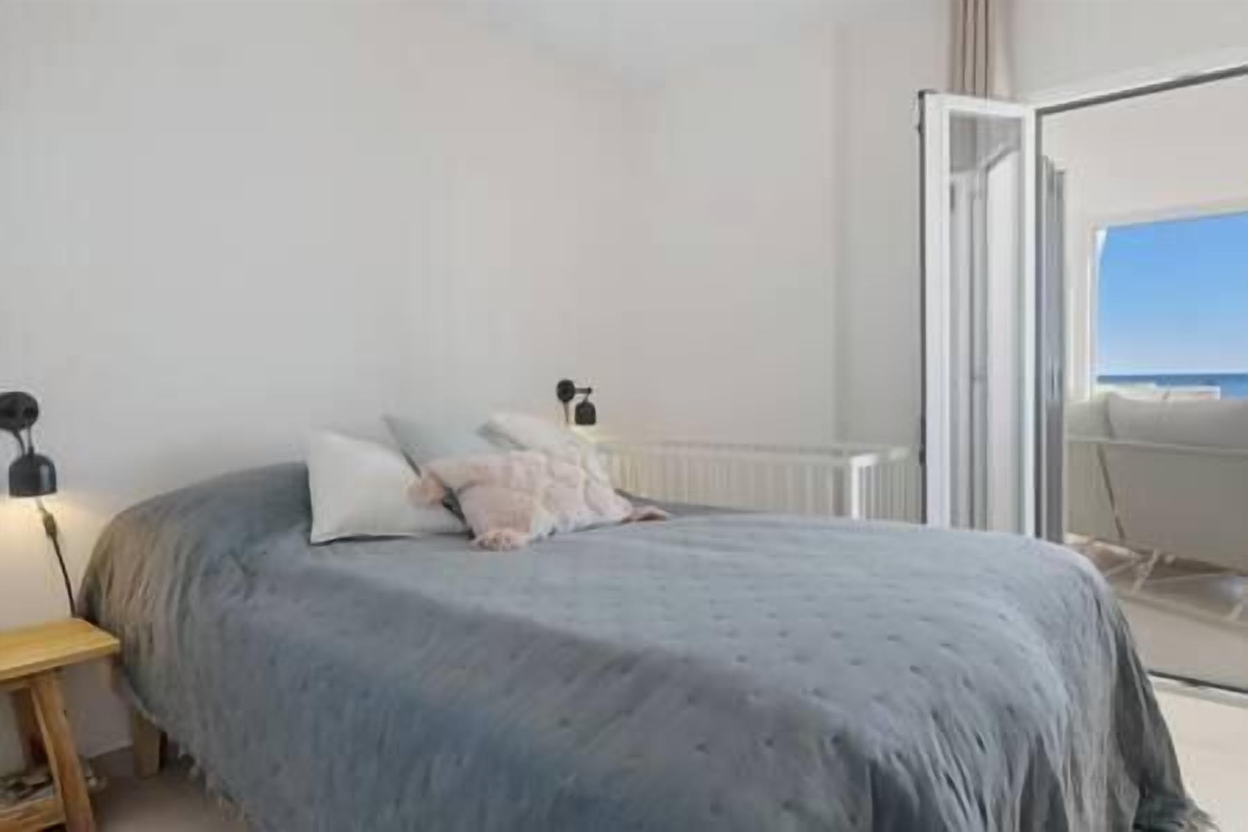 A bedroom with a bed, a nightstand, and a view of the outdoors.