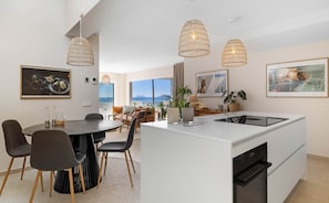 A modern kitchen with a central island, dining area with chairs, pendant lights, and artwork on the walls. - Bermeja Beach | Ref. #54 (Estepona)