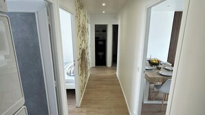 A hallway with a wooden floor, white walls, and a dining area with a table set for two. - Spacious 3-bedroom near Paris - Private parking (Aubervilliers)