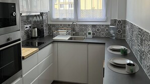 A modern kitchen with white cabinets, a built-in oven, a sink, and a window with curtains. - Spacious 3-bedroom near Paris - Private parking (Aubervilliers)