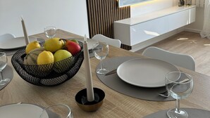 A modern dining area with a TV mounted on the wall, a fruit bowl on the table, and a candle. - Spacious 3-bedroom near Paris - Private parking (Aubervilliers)