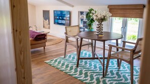 A dining area with a round table, two chairs, a vase with flowers, and a view of the outdoors through a window. - Rustic Barn Retreat in North Dorset (Gillingham)