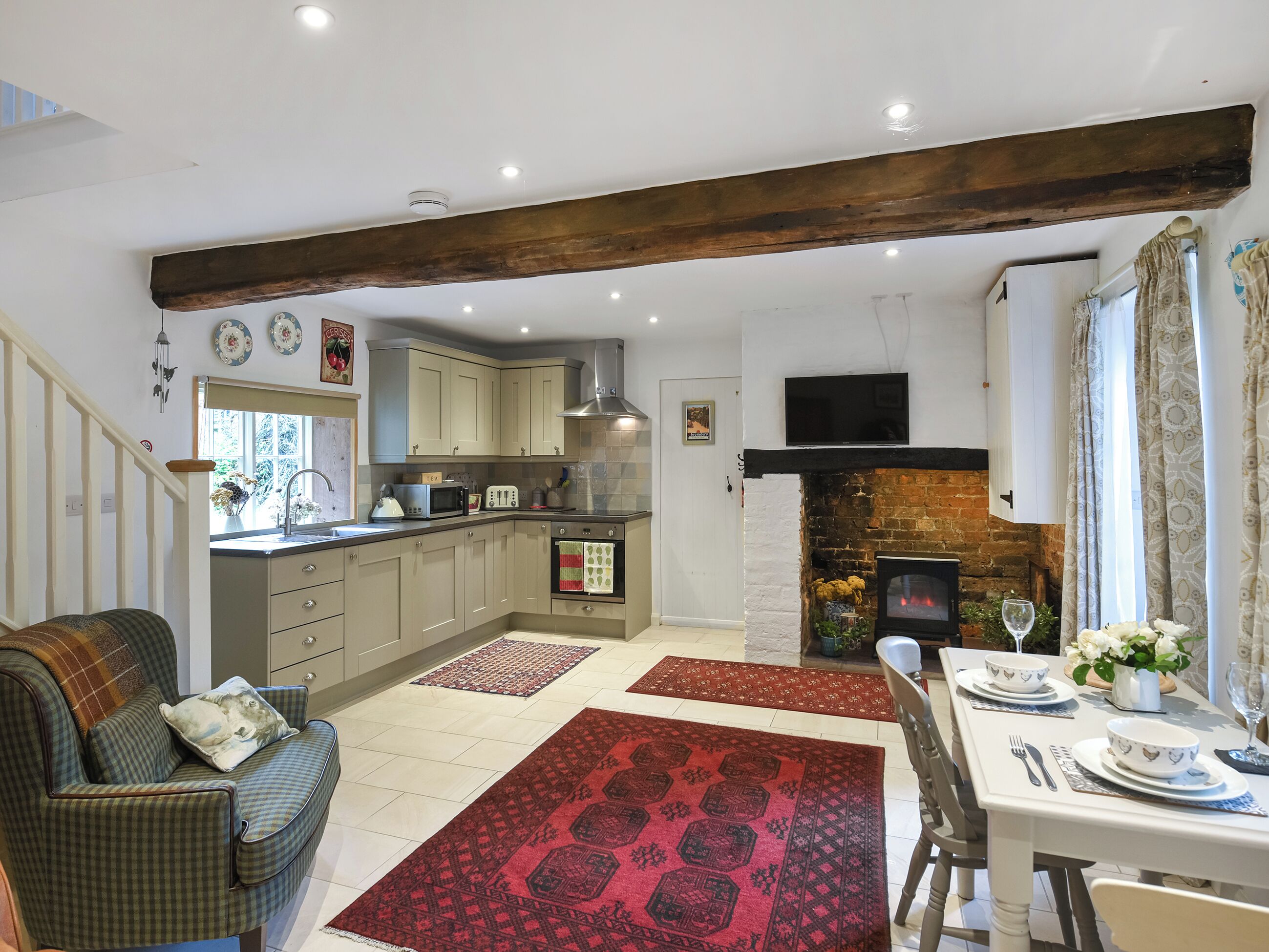 A cozy kitchen with wooden beams, a dining area with a table set for two, and a fireplace.