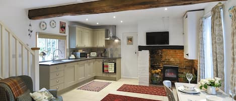 Una cocina acogedora con vigas de madera, un rincón comedor con una mesa dispuesta para dos personas y una chimenea.