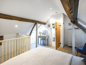 Un dormitorio con techo inclinado, una viga de madera, cama, escritorio y armario.