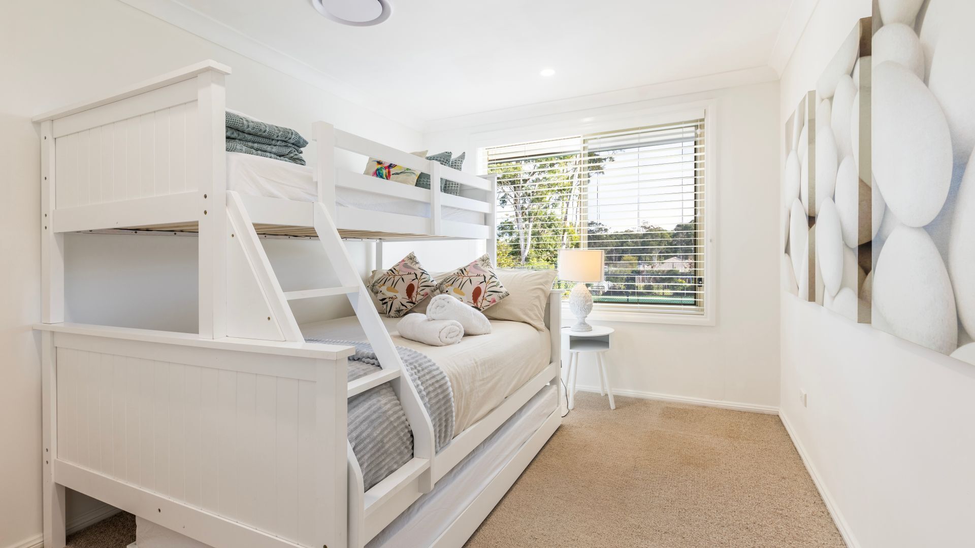 A bunk bed room with a window, a small table, and a lamp.