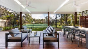 A covered outdoor seating area with a view of a tennis court and greenery. - Anglesey - Pet Friendly with Pool - 4 Mins Walk to Beach (Callala Bay)