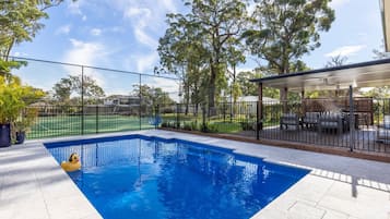 Una piscina con un deck cercado, rodeada de árboles y una zona de estar cubierta.