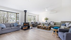 A modern living room with a wood-burning stove, grey sofas, a coffee table, and large windows. - Anglesey - Pet Friendly with Pool - 4 Mins Walk to Beach (Callala Bay)