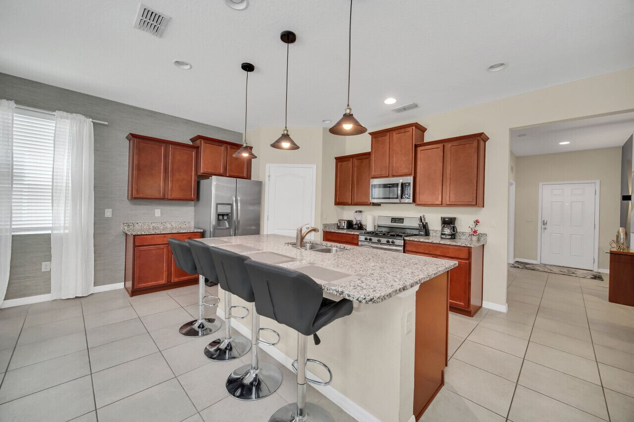 A modern kitchen with wooden cabinets, a central island with bar stools, stainless steel appliances, and pendant lighting.