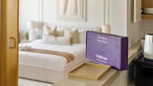 A hotel room with a bed, a bedside table, a purple sign, and a wooden tray. - Silkhaus AL Sana 2 - AL Raha (Abu Dhabi)