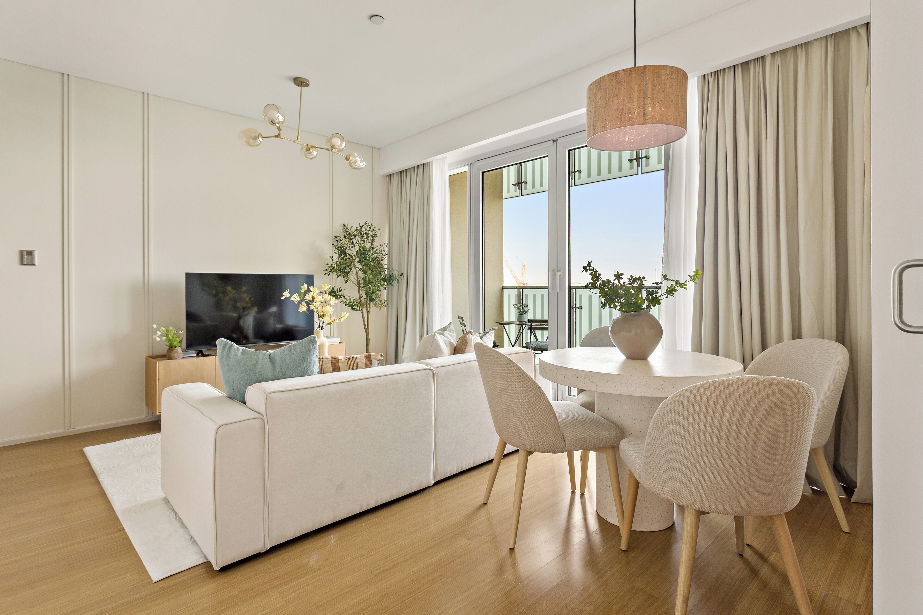 A modern living room with a sofa, TV, dining table, chairs, and a large window with curtains.