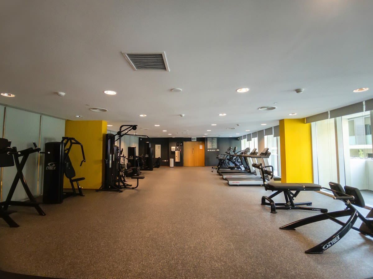 A gym with cardio machines, weightlifting equipment, and a yellow accent wall.