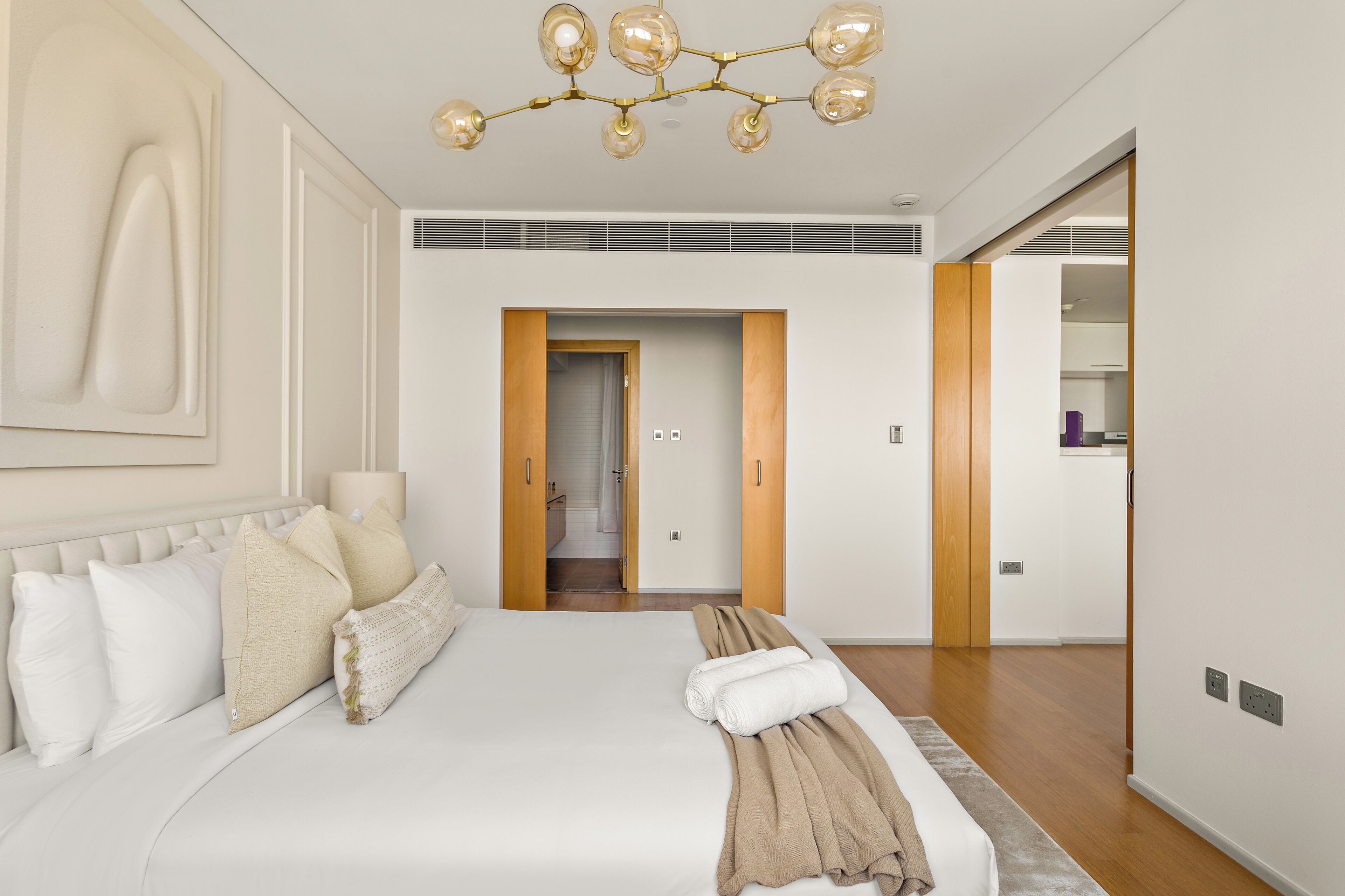 A hotel room with a large bed, a chandelier, a wooden door, and a view of the bathroom.
