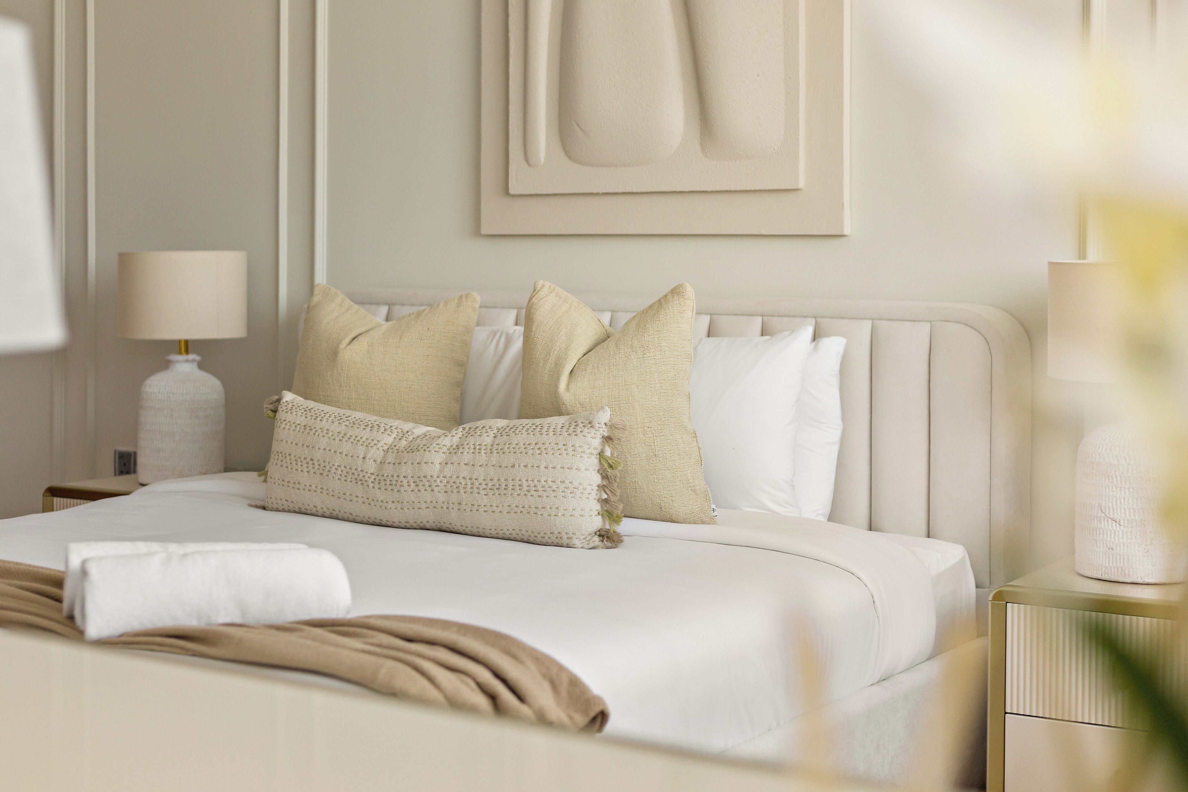 A neatly made bed with a white duvet, beige and white pillows, and a beige throw blanket.