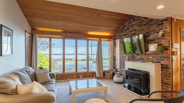 A cozy living room with a sofa, coffee table, and chairs, a fireplace, and a TV mounted on a brick wall.