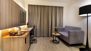 Une chambre d’hôtel moderne avec un bureau en bois, un canapé, une petite table ronde ornée d’un vase et une lampe sur pied.