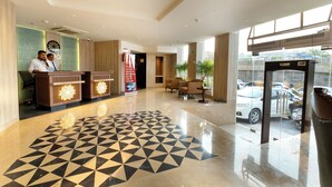 Un hall d’hôtel doté d’un sol à motifs géométriques, de comptoirs d’accueil, d’une grande fenêtre et d’une vue sur les voitures garées à l’extérieur.