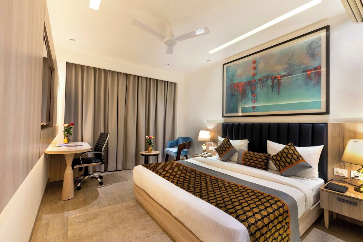 A hotel room with a large bed, a desk, a chair, a nightstand, and a ceiling fan.