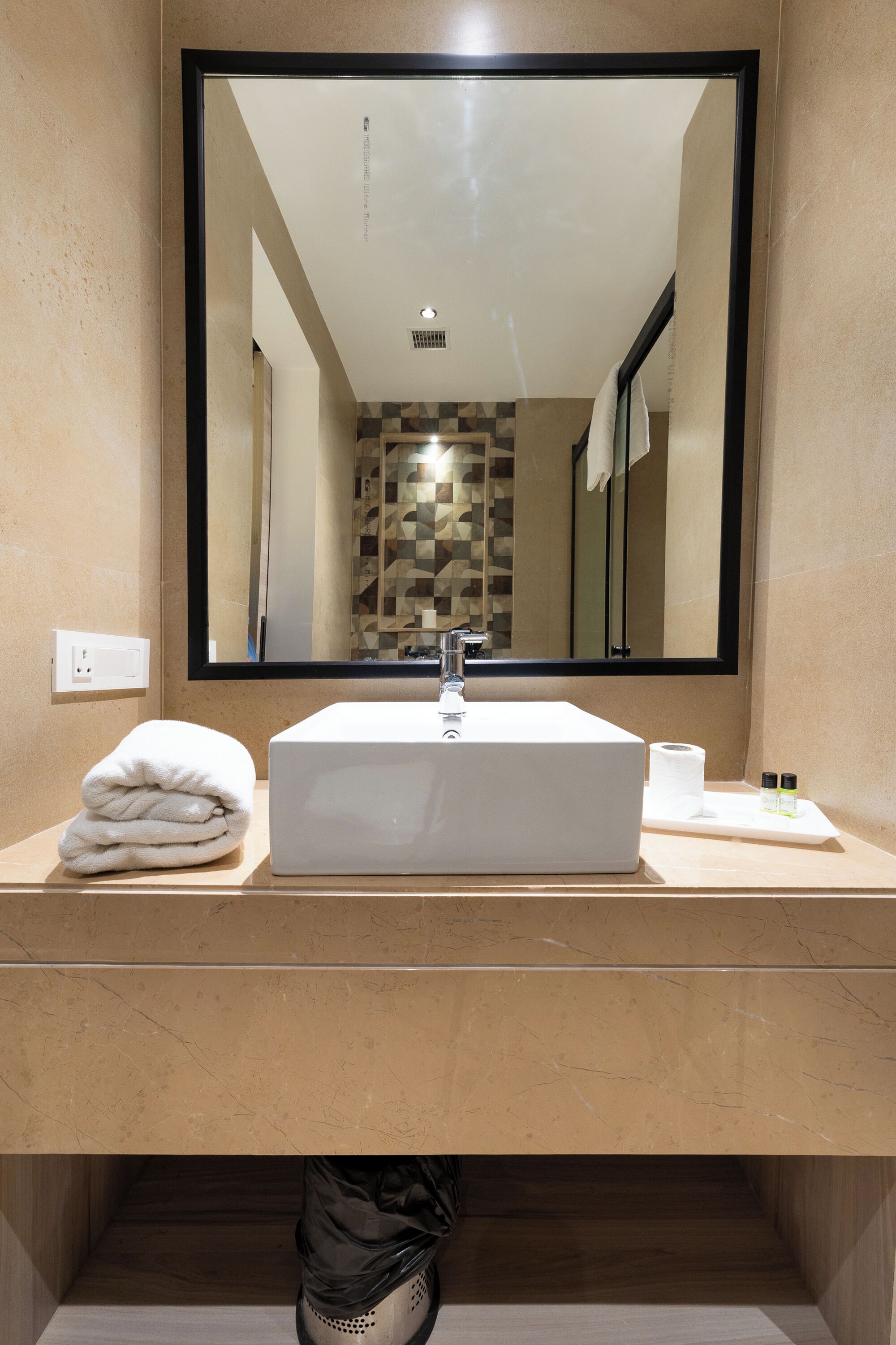 Un bagno con uno specchio grande, un lavandino bianco, un asciugamano, carta igienica e articoli da toilette.