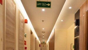 Un couloir d’hôtel avec un motif géométrique sur le sol, un panneau indiquant le sens des ascenseurs et un téléphone fixé au mur.