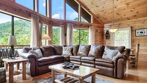 A cozy cabin interior with a large leather sectional sofa, a wooden coffee table, and a rustic rug. - Cozy Private Cabin with Hot Tub & Mountain Views (Sevierville)