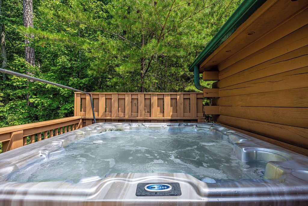 Un jacuzzi con una terraza de madera y una cabaña al fondo.