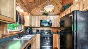 A kitchen with wooden cabinets, a black refrigerator, a stove, and a sink. - Cozy Private Cabin with Hot Tub & Mountain Views (Sevierville)