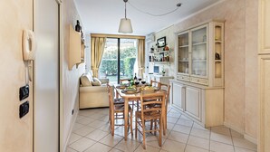 A dining area with a wooden table and chairs, a sofa, and a kitchen with cabinets and a window. - Residence Villa Giulia 5-03 with pool by Wonderful Italy (Desenzano del Garda)