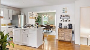 Une cuisine moderne avec des meubles blancs, un îlot central et un coin repas comprenant une table et des chaises en bois.