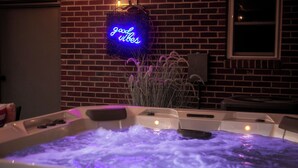 Un jacuzzi avec jets d’eau, un panneau lumineux néon affichant le message « bonne ambiance », et un mur de briques.