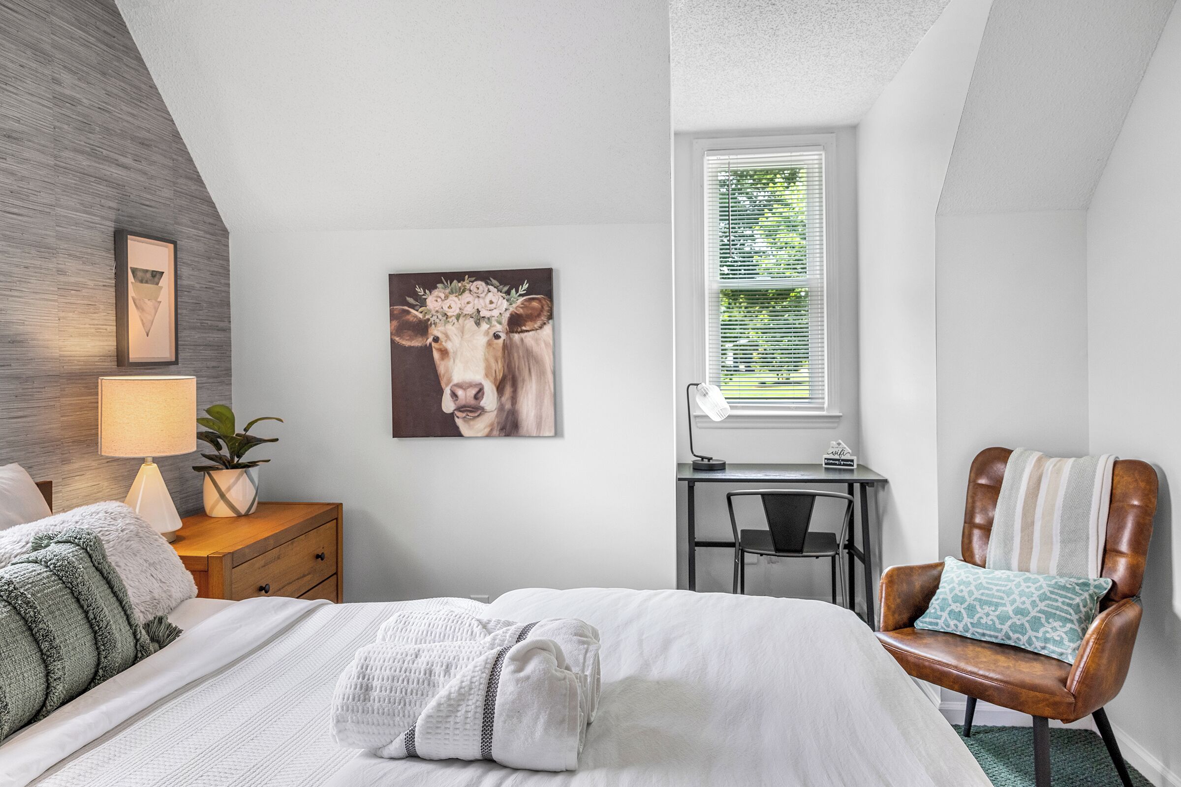 A bedroom with a bed, a desk, a chair, and a window with blinds.