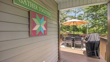 A covered outdoor area with a sign that reads "GATHER TOGETHER," a colorful geometric artwork, outdoor furniture, and a grill on a deck.
