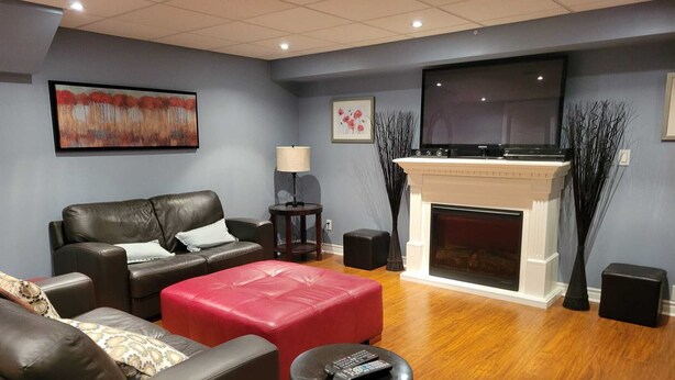A modern living room with a fireplace, leather sofas, a red ottoman, a TV, and a lamp.
